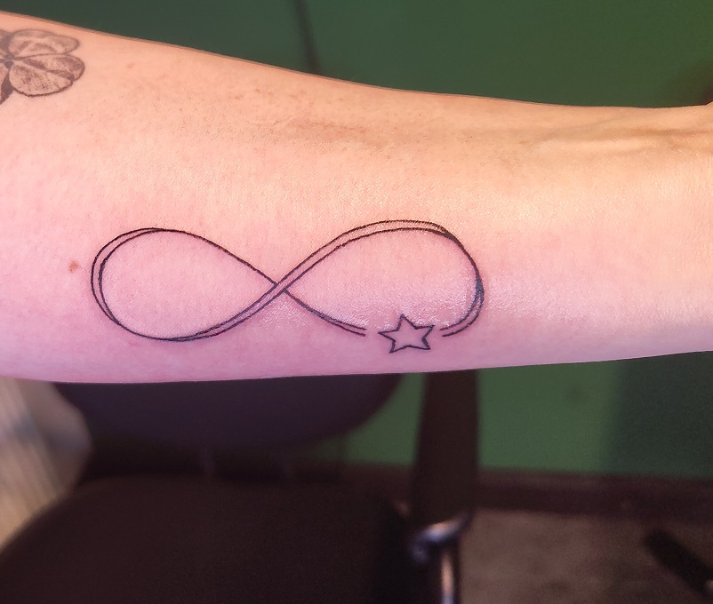 Tattoo eines Unendlichkeitszeichens mit einem kleinen Stern auf dem Unterarm