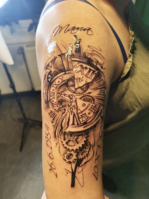 Tattoo eines zersprungenen Uhr mit Geburts und Sterbedatum und der Schrift 'Mama' auf dem Oberarm